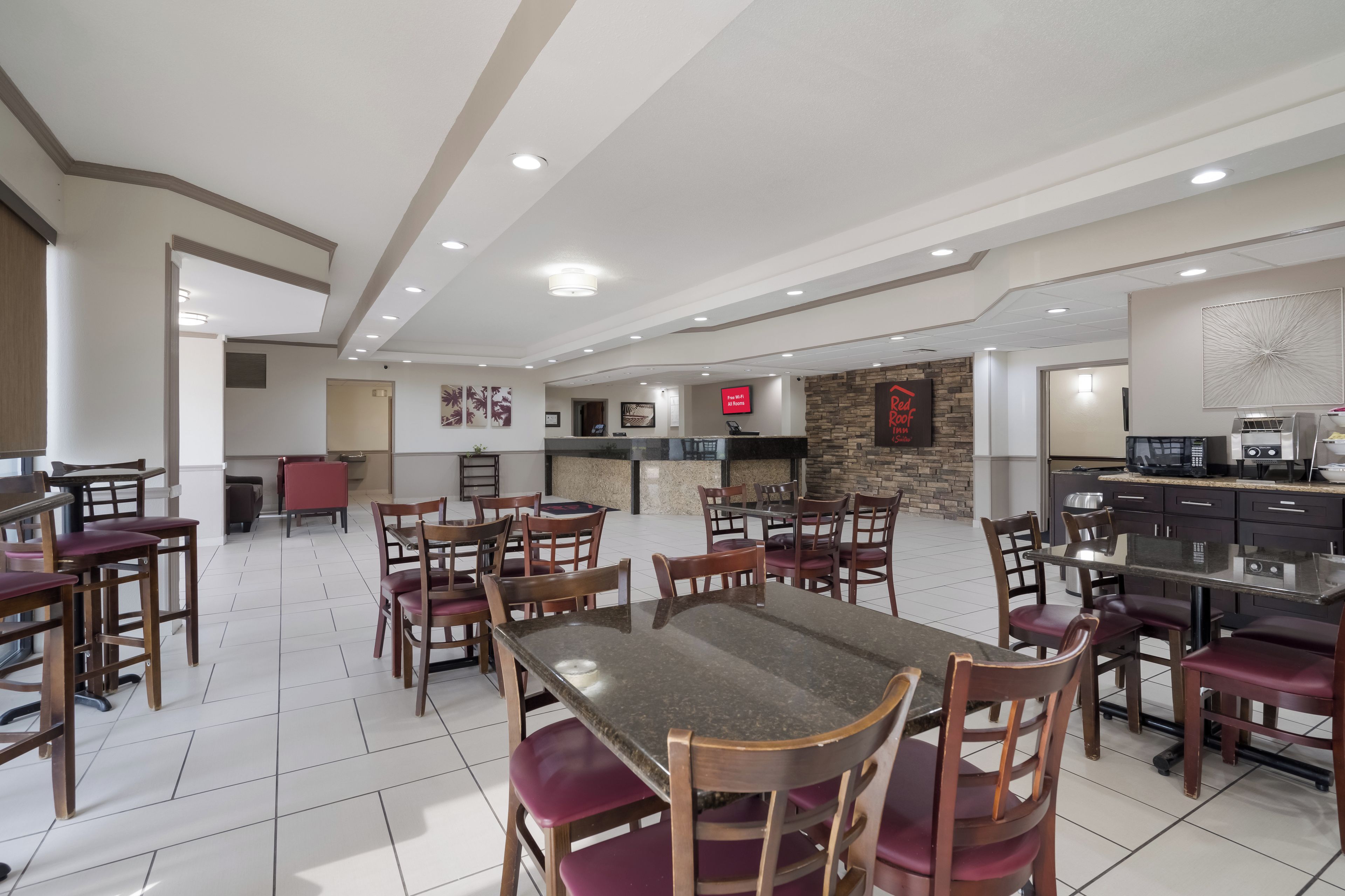 A hotel dining area with multiple tables and chairs, a kitchen area with appliances, and a reception desk.