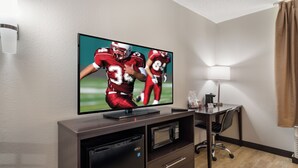 Een hotelkamer met een flatscreen televisie bevestigd aan een houten kast, een bureau met een lamp en een stoel.
