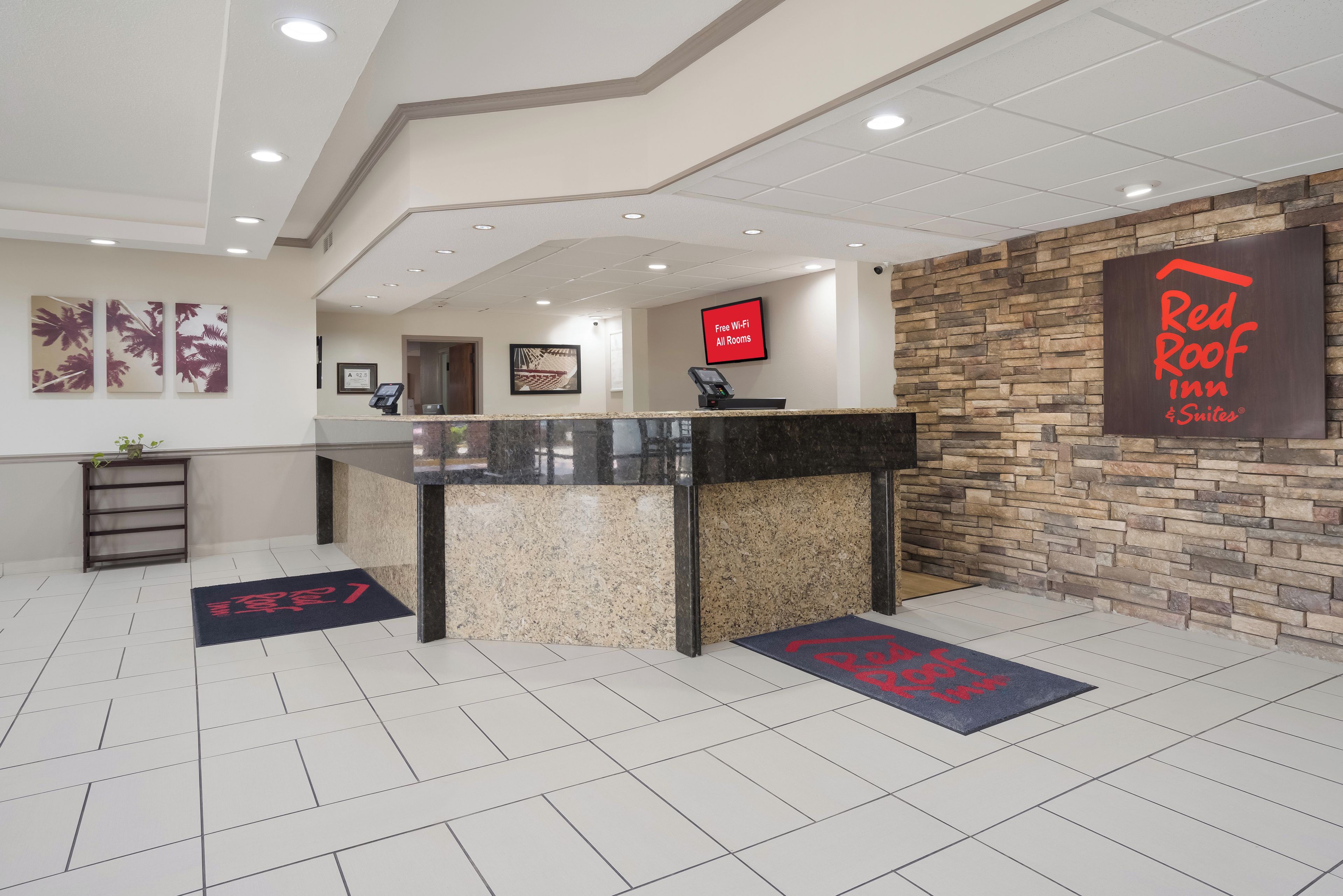 A hotel reception area with a reception desk, a digital screen, and a stone wall.