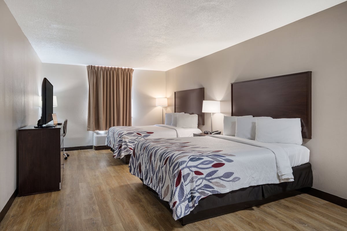 Une chambre d’hôtel avec deux lits, un bureau, une télévision et une fenêtre avec des rideaux.
