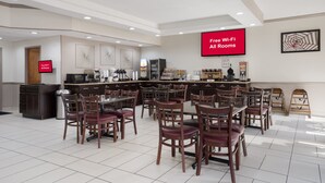 Un hall de hotel con comedor, cocina y una pantalla grande que muestra “Wi-Fi gratuito en todas las habitaciones”.