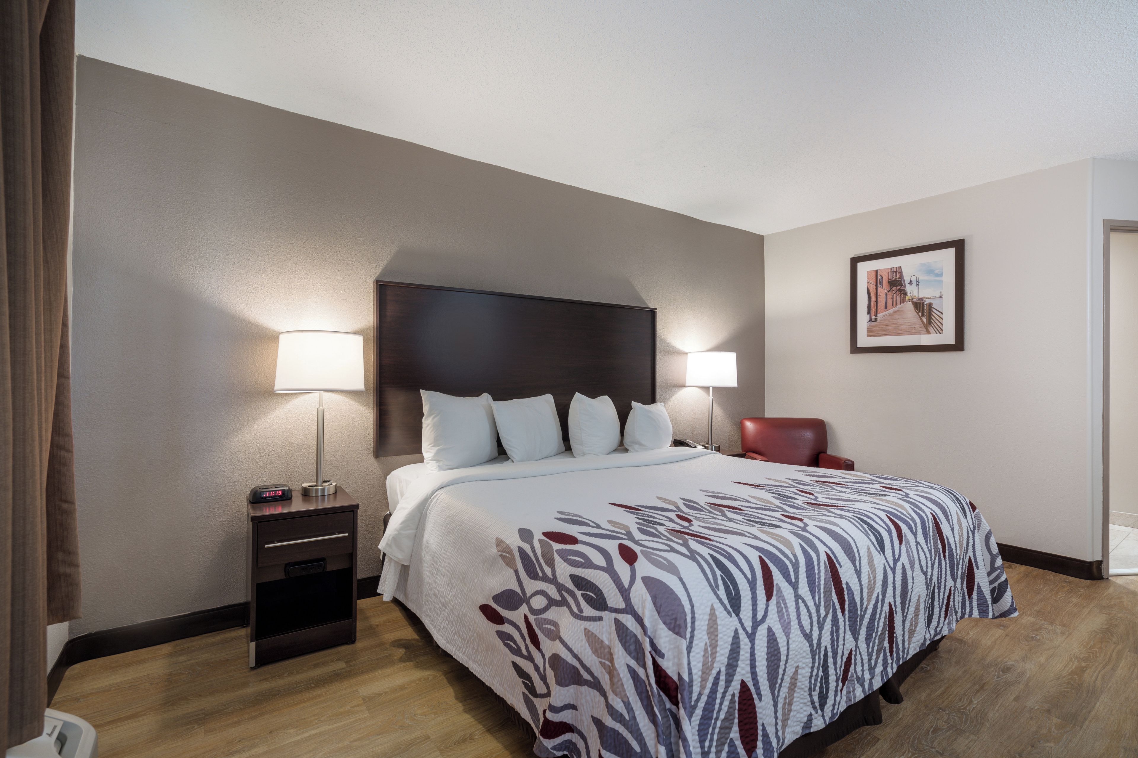 A hotel room with a bed, bedside lamps, a chair, a nightstand, and a framed picture on the wall.