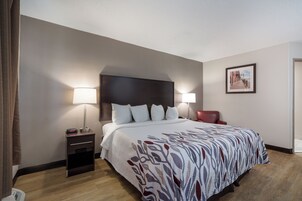 Una habitación de hotel con cama, lámparas de noche, una silla, mesita de noche y un cuadro en la pared.