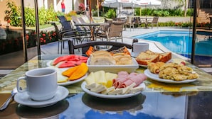 A breakfast table with various food items, a cup, and a poolside setting with umbrellas and chairs.