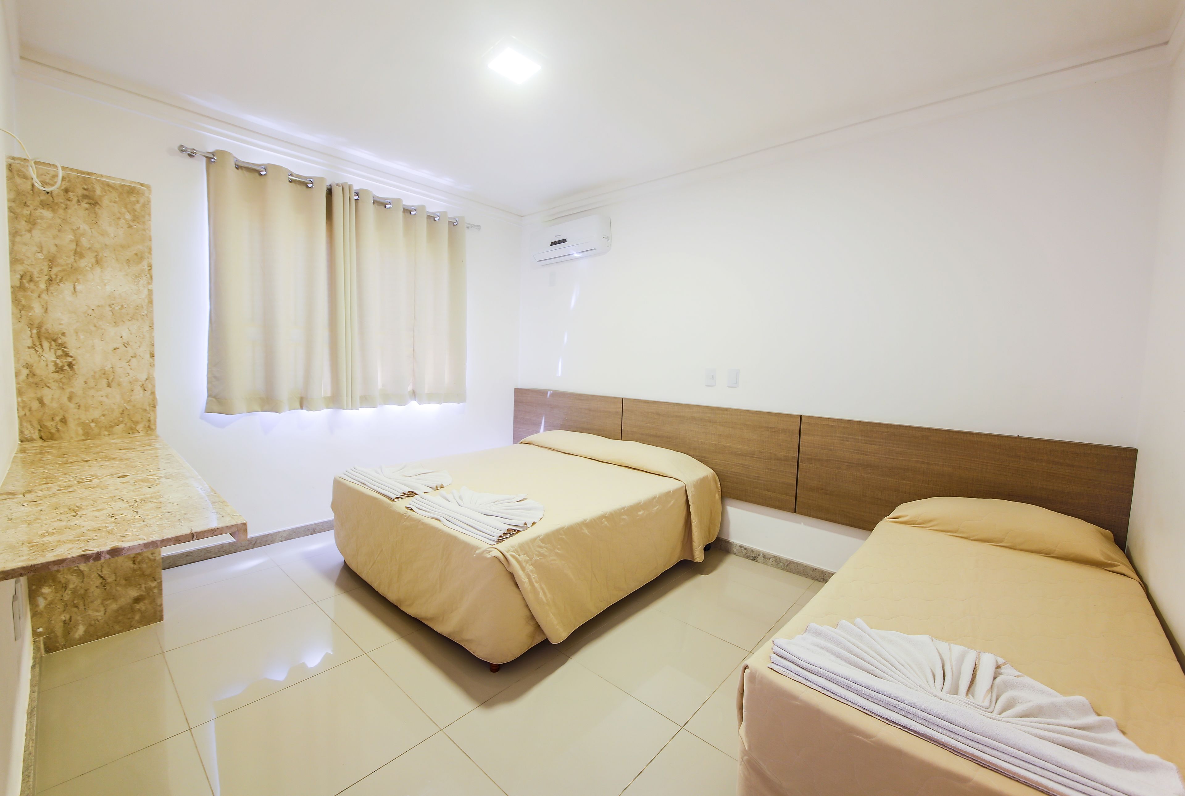 Una habitación de hotel con cama, un banco y una ventana con cortinas.
