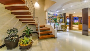 A modern interior with a wooden staircase, potted plants, and a well-lit area with a counter and chairs.