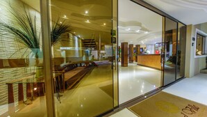 A modern hotel lobby with a reception desk, seating area, and a large plant.