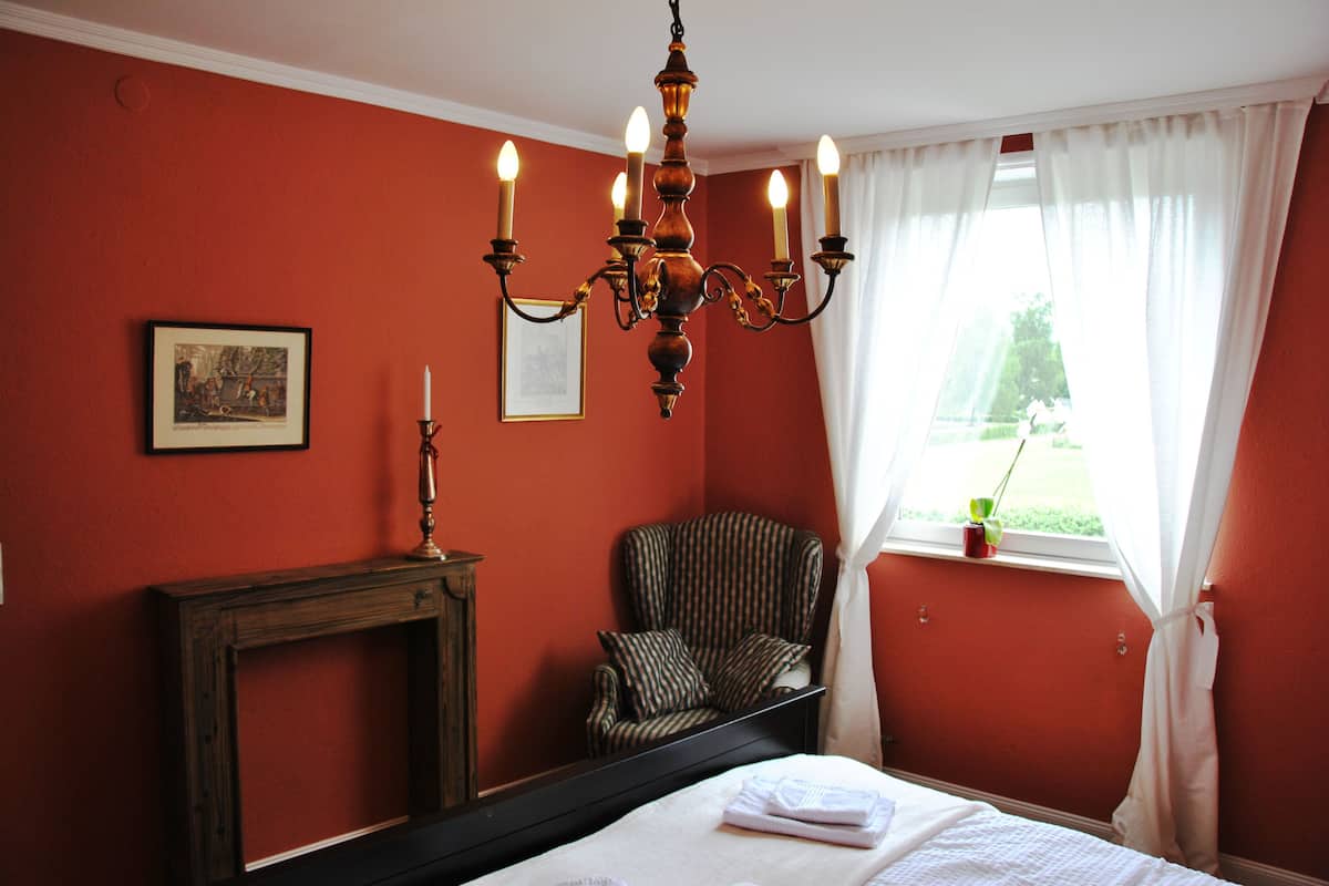 A bedroom with a bed, a chair, a fireplace, and a window with curtains.