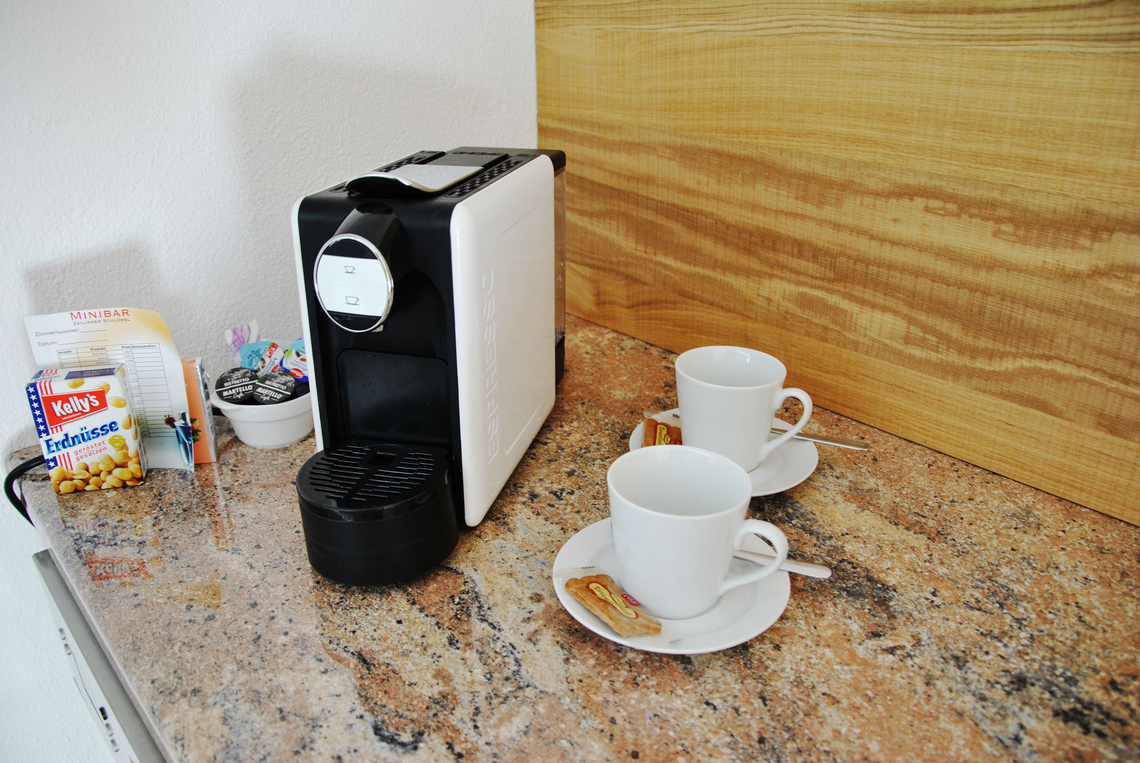 A kitchenette with a coffee maker, two cups, a box of Kellogg's cereal, and a small bowl.