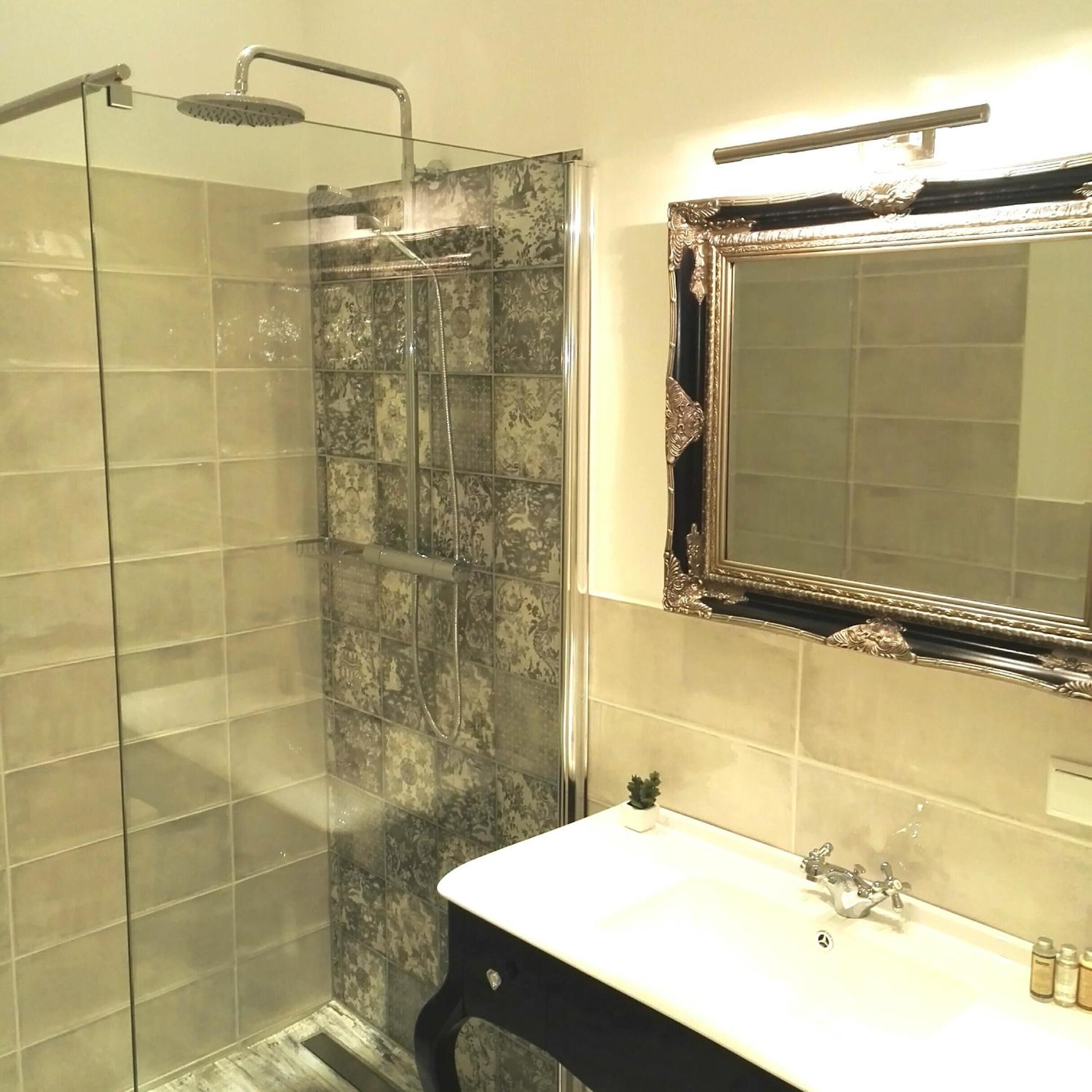 Un baño con cabina de ducha de vidrio, un lavabo con mueble negro y un espejo con marco ornamentado.