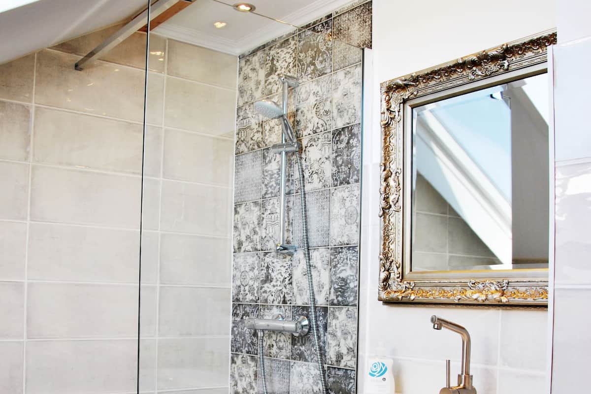 A modern bathroom with a glass shower enclosure, a white vanity with a gold faucet, and a decorative mirror.