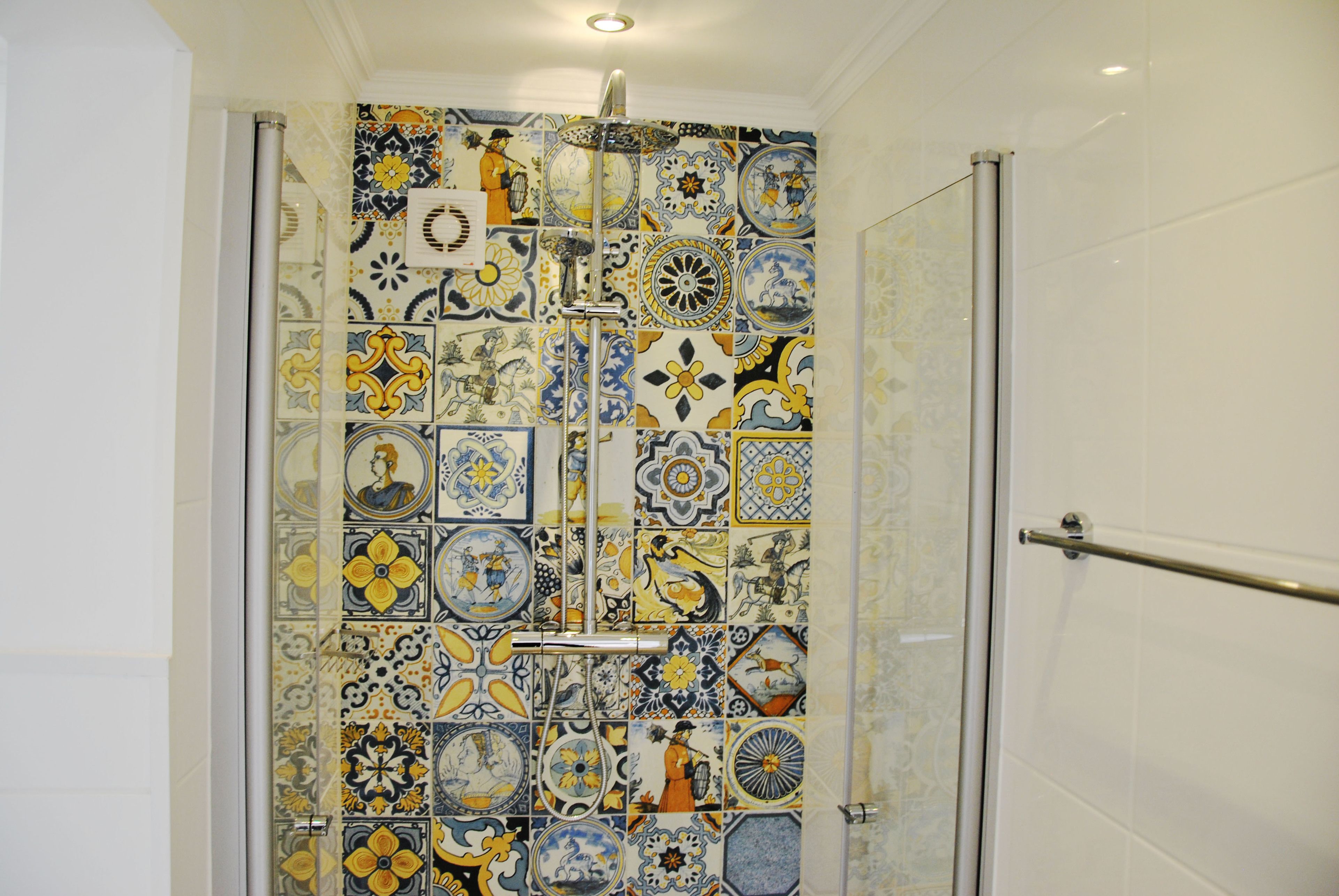 A bathroom with a tiled shower wall featuring a variety of patterns and designs.