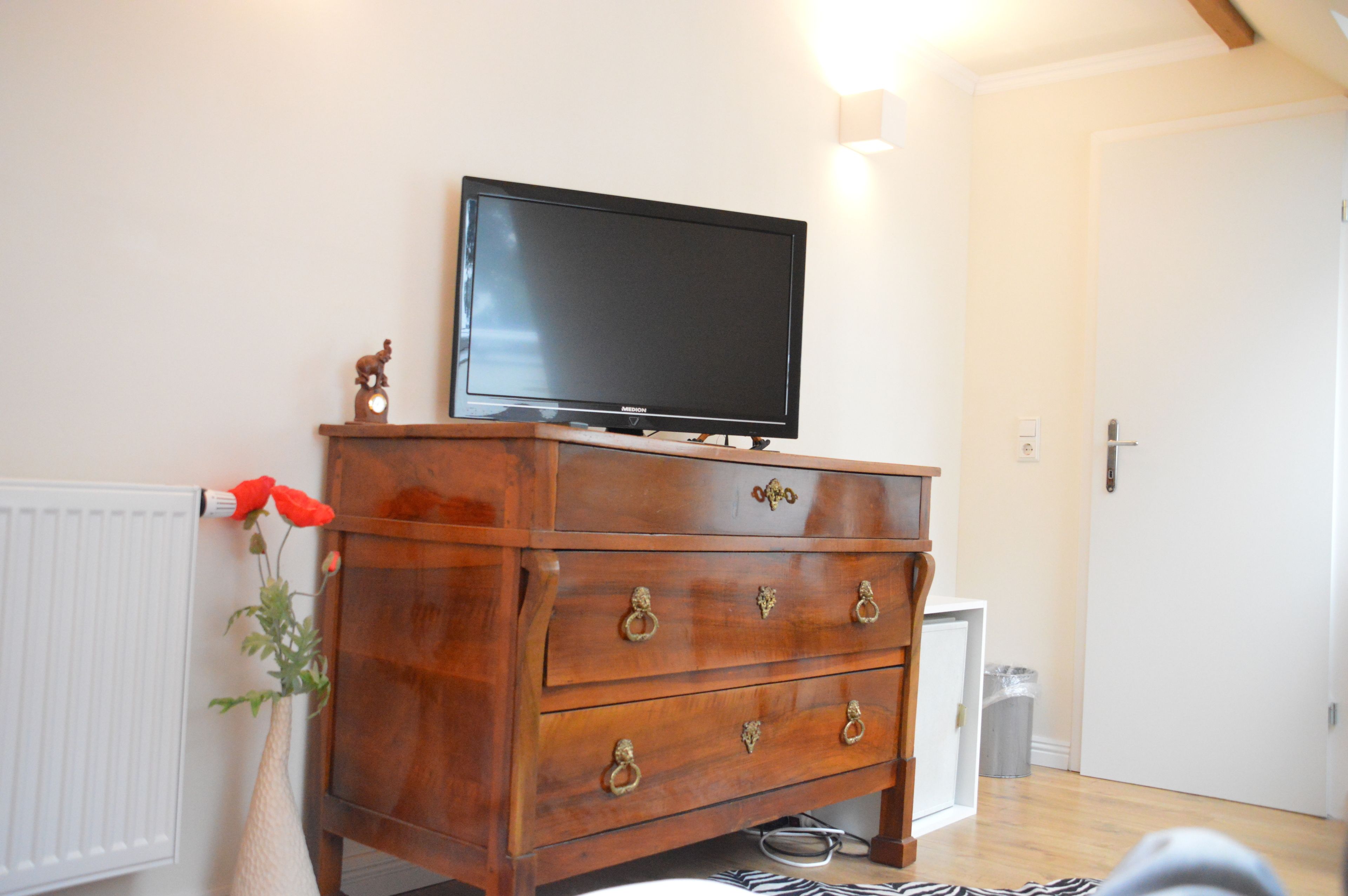 A wooden dresser with a television on top, a radiator, and a trash bin.