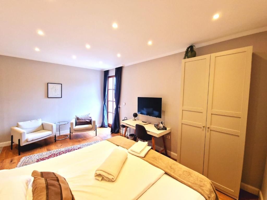 Habitación de hotel con cama, escritorio con computadora, televisor, armario y zona de estar con sofá y sillones.