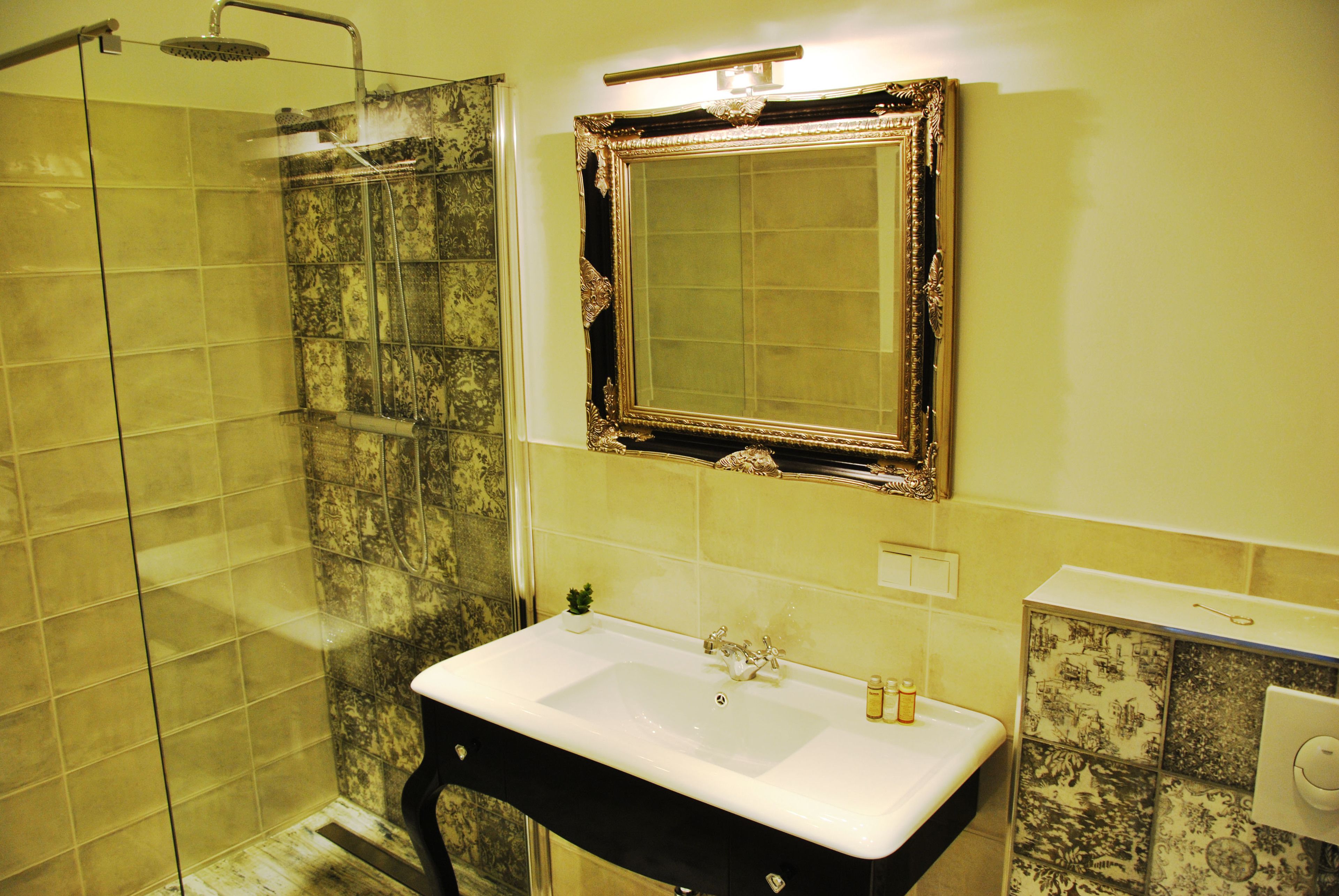 A bathroom with a glass shower enclosure, a sink with a decorative mirror above it, and patterned tiles on the walls.