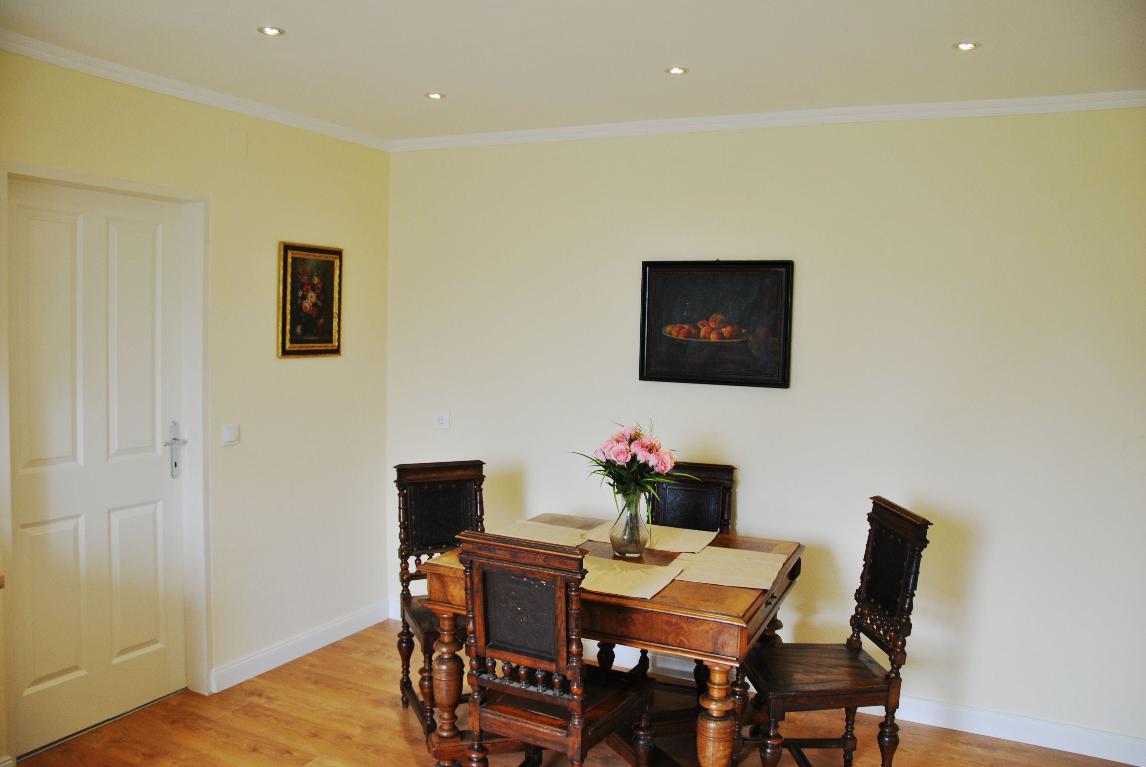 A dining room with a wooden table, chairs, and a vase of flowers.