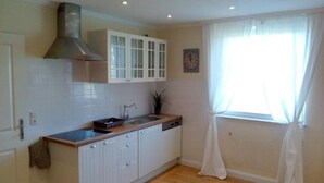 A kitchen with white cabinets, a stainless steel range hood, a sink, and a window with sheer curtains. - Gutshaus beim Zeilinger Schlössl (Knittelfeld)