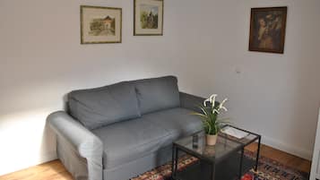 Ein Wohnzimmer mit einem grauen Sofa, einem Glastisch mit einer Pflanze und drei gerahmten Kunstwerken an der Wand.