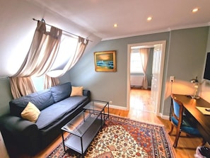 A living room with a sofa, coffee table, and a patterned rug. There is a painting on the wall and a door leading to another room. - Gutshaus beim Zeilinger Schlössl (Knittelfeld)