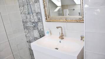 Un baño con un lavabo blanco, un espejo con marco dorado y una zona de ducha con azulejos estampados.