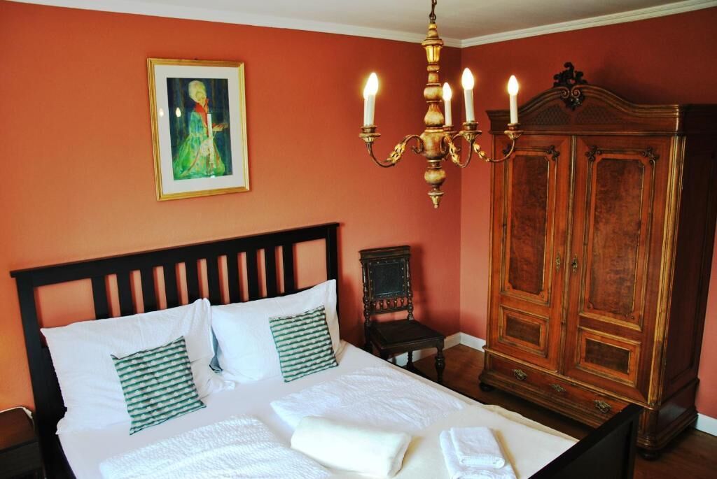 Una cama con sábanas blancas, una almohada verde y blanca a rayas, y un cuadro en la pared.