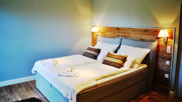 A neatly made bed with pillows and a blanket, a wooden headboard, and two bedside lamps. - Gutshaus beim Zeilinger Schlössl (Knittelfeld)