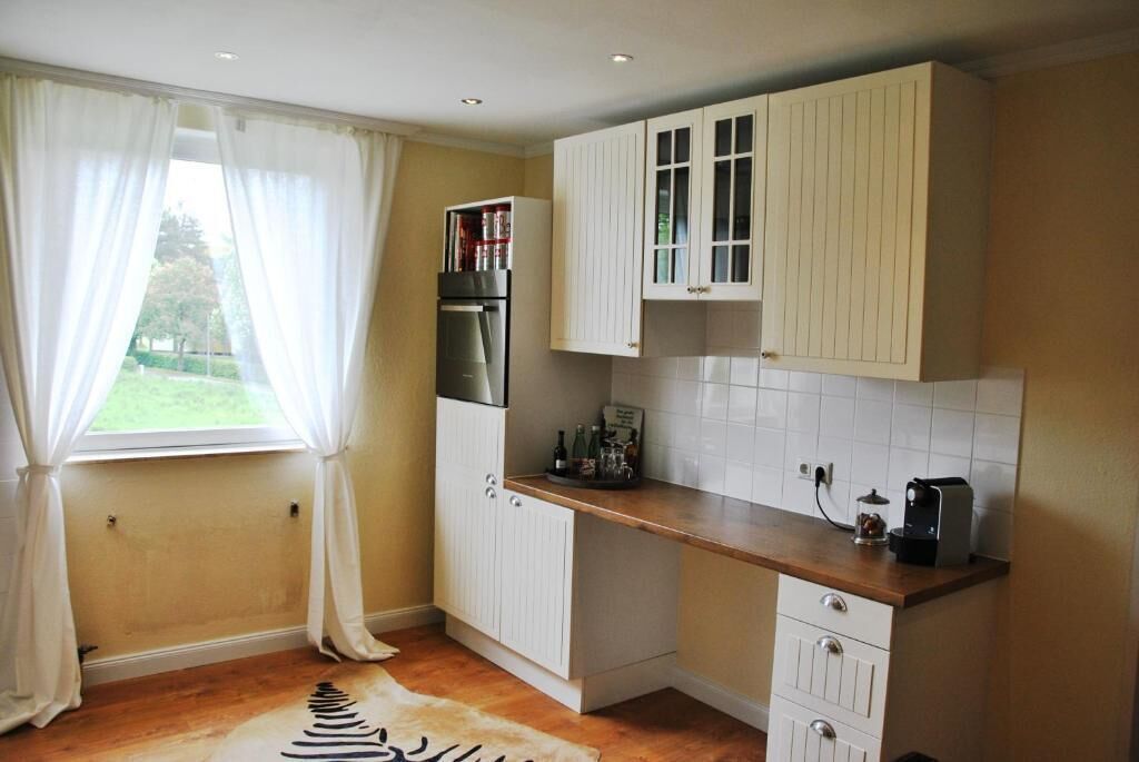 A compact kitchen with white cabinetry, a built-in oven, and a countertop with a coffee maker.