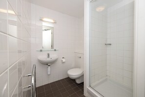 Une salle de bain moderne avec des carreaux blancs, une douche en verre, un lavabo et des toilettes.