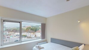 A bedroom with a large window, a bed, and a view of a street and buildings. - Victoria Mills (Cork)