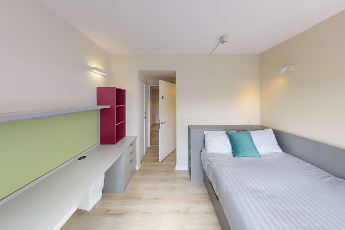Un dormitorio con cama, un banco, un armario y una puerta que da a otra habitación.