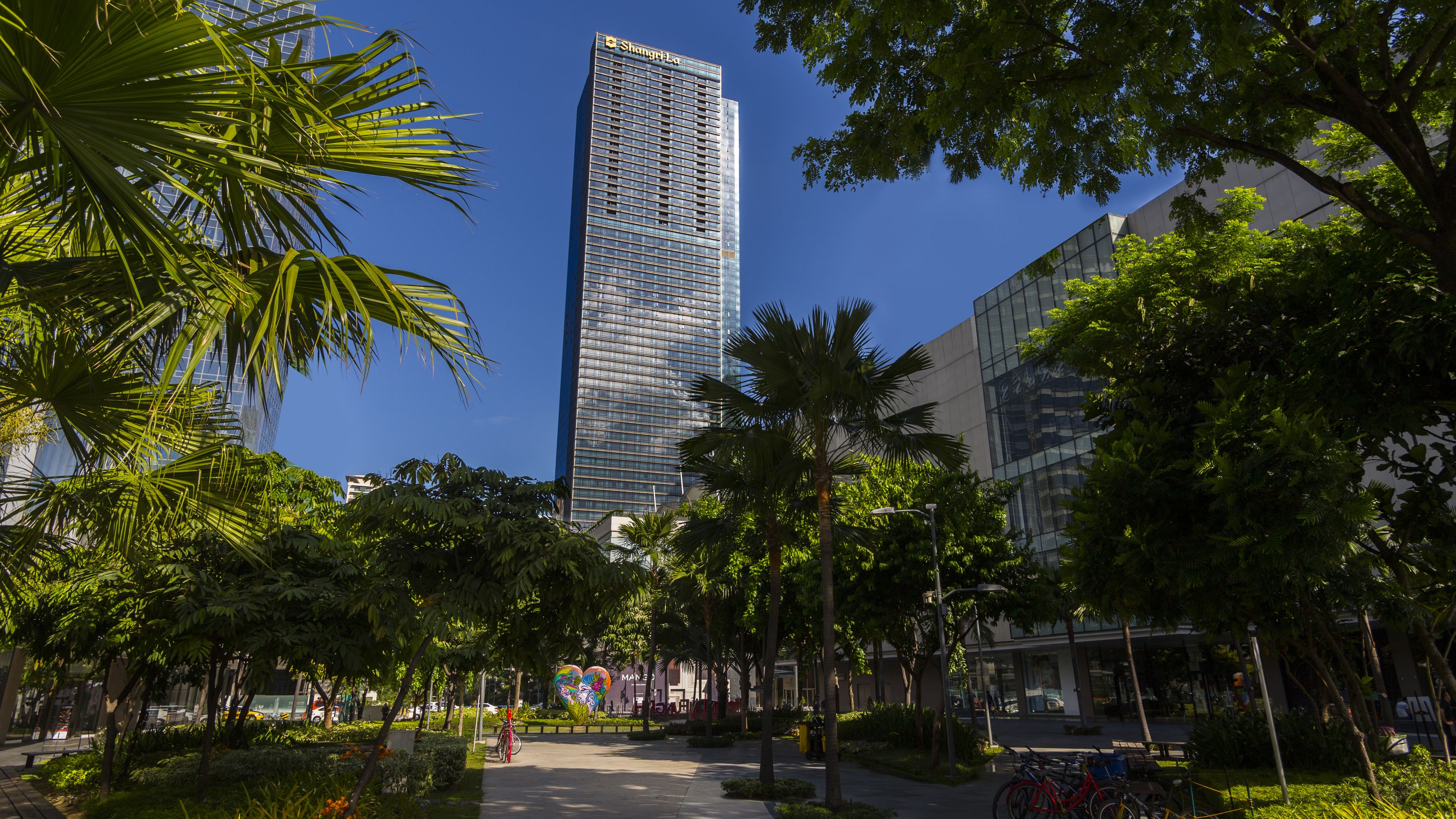A modern building with a glass facade, surrounded by lush greenery and a clear blue sky.
