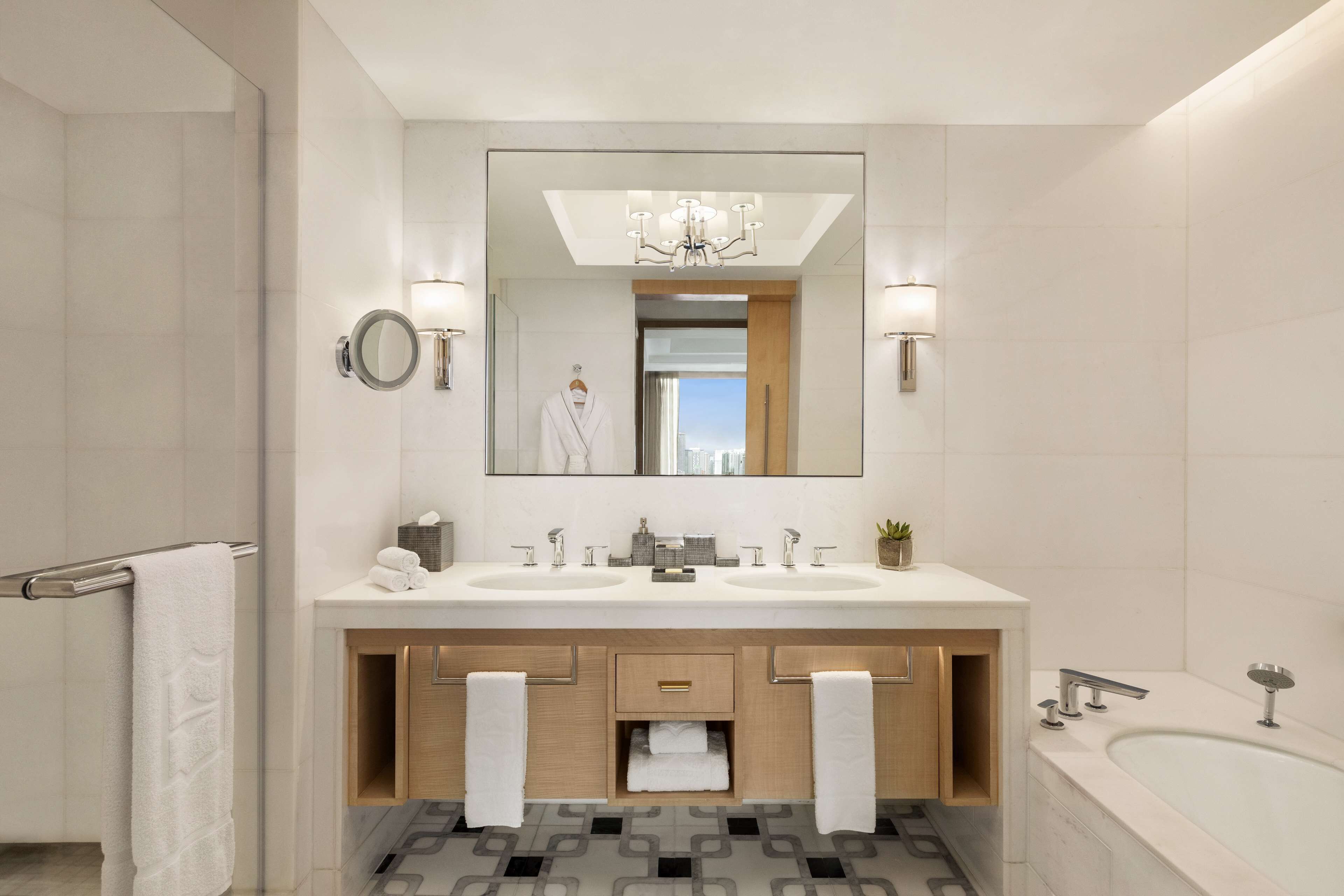 Un baño moderno con un espejo grande, dos lavamanos, una bañera y un perchero para toallas.