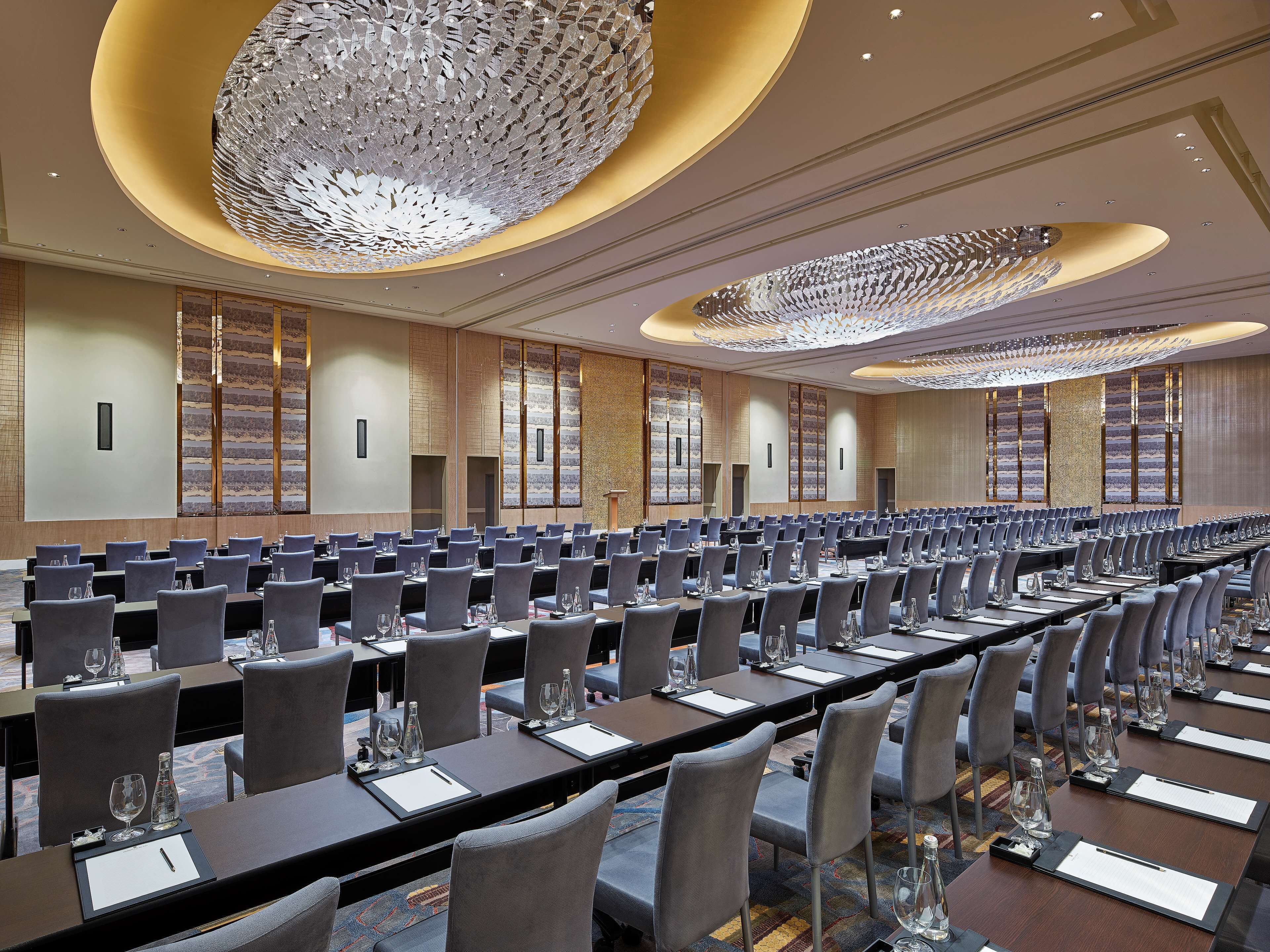 A large conference room with rows of tables and chairs, a modern chandelier, and a large window with a view.