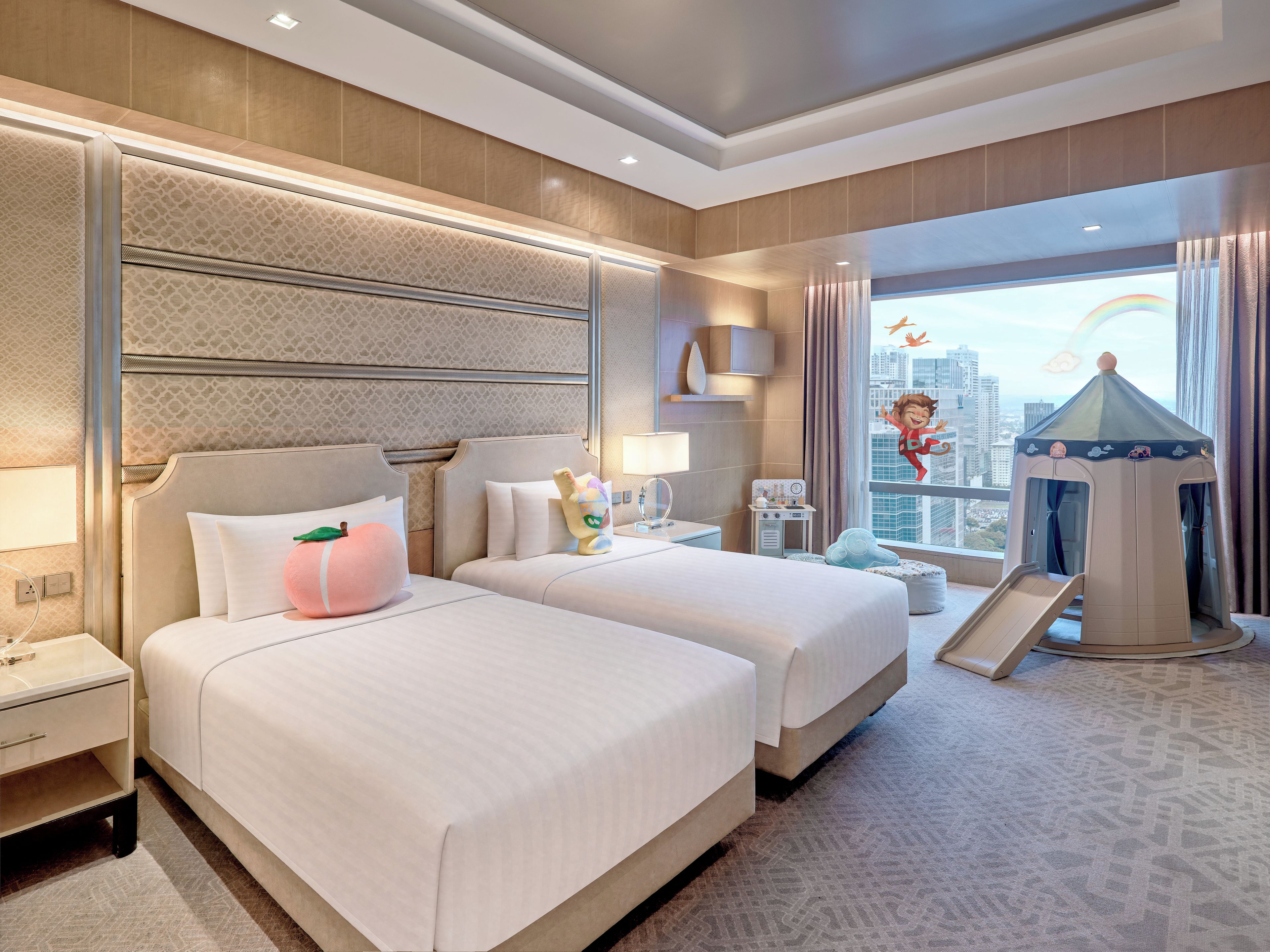 A hotel room with two beds, a children's play area, and a view of the city.