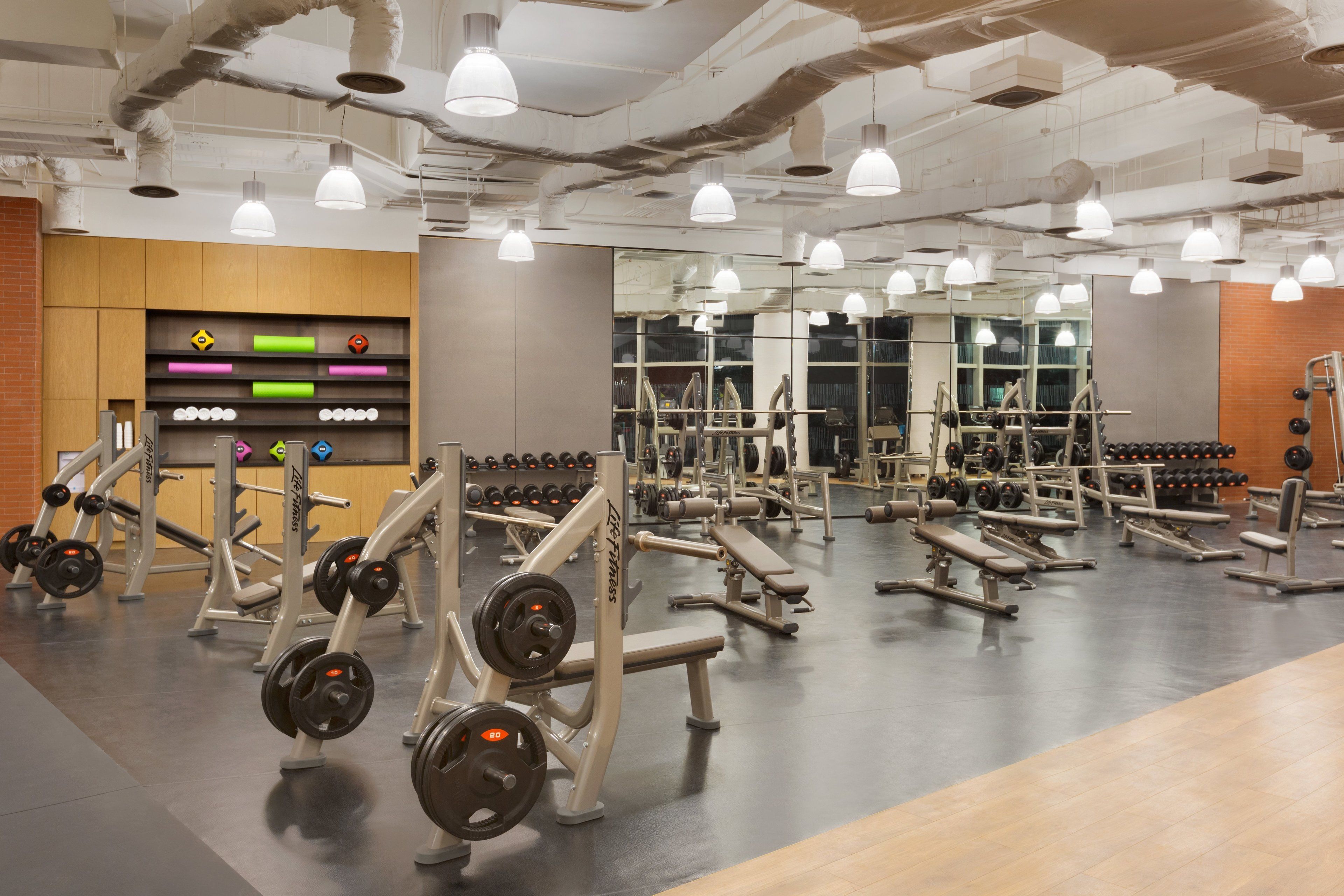 Un gimnasio con equipo de levantamiento de pesas, espejos e iluminación colgante.
