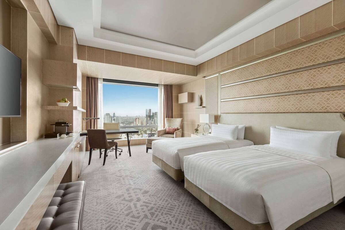 A hotel room with a large bed, a desk, a chair, and a view of the city.