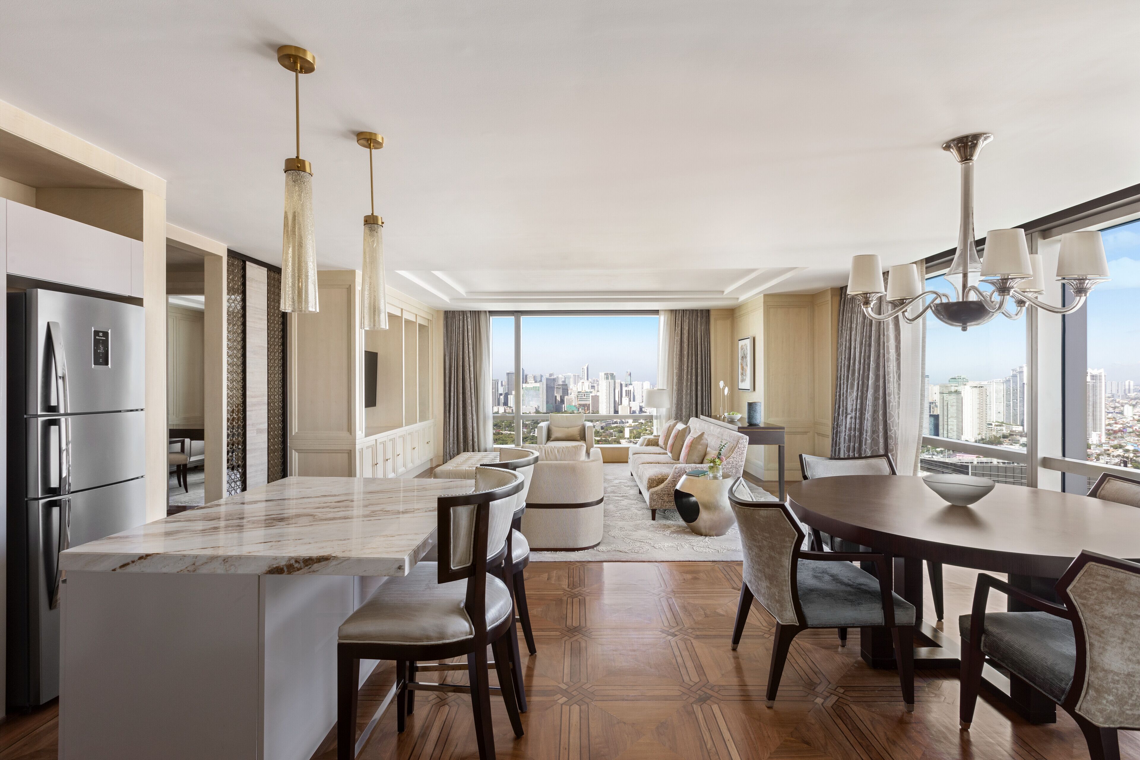 A modern kitchen with a marble island, dining area with a round table, and a view of the city.