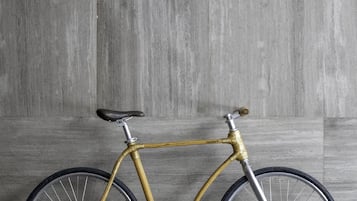 A bamboo bicycle with a black seat and silver handlebars against a grey concrete wall.