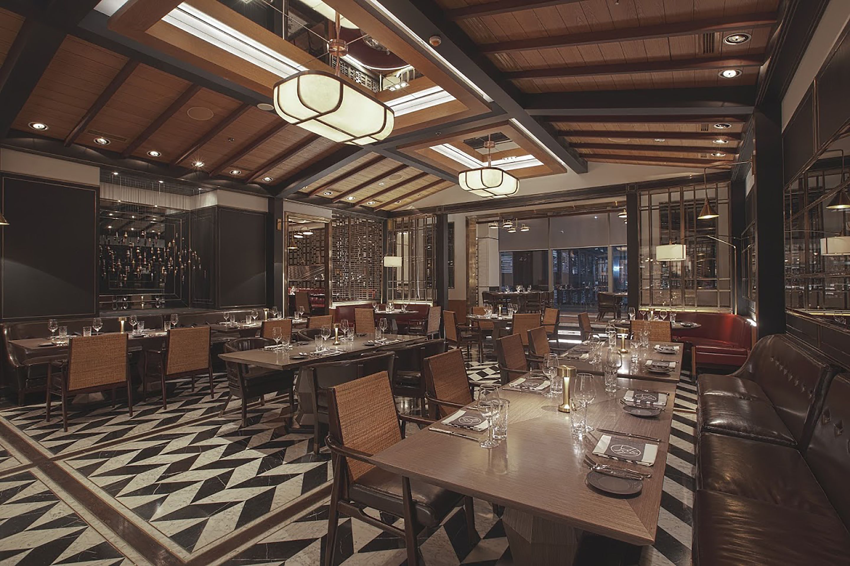 A spacious dining area with high ceilings, wooden beams, and modern pendant lighting. Tables are set with fine china and glassware.