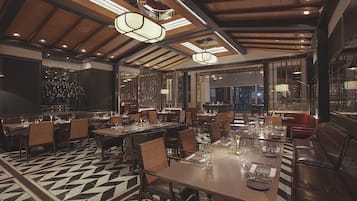 A spacious dining area with high ceilings, wooden beams, and modern pendant lighting. Tables are set with fine china and glassware.