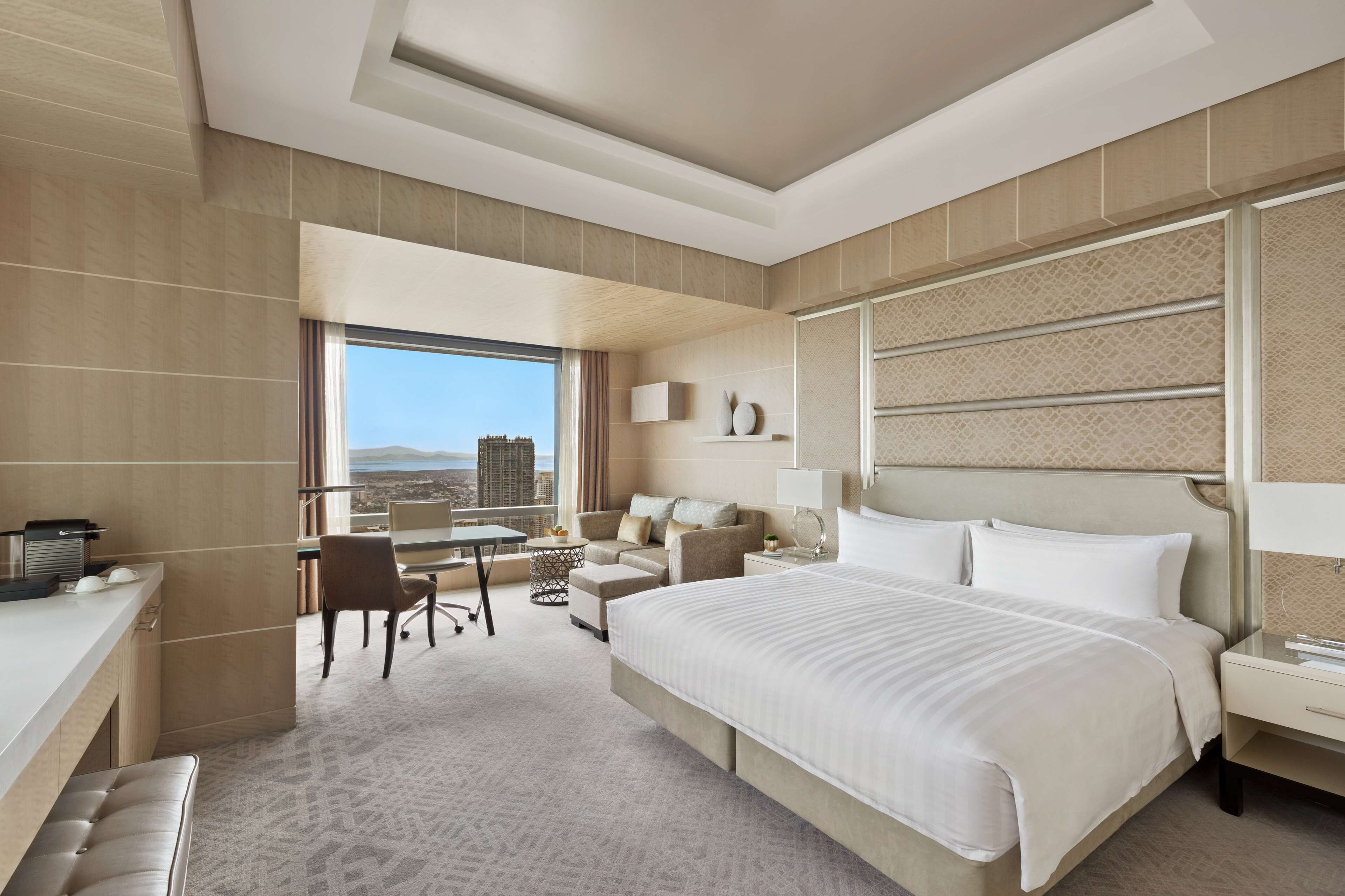 Ein modernes Hotelzimmer mit einem großen Bett, einem Schreibtisch, einem Sessel und Blick auf die Stadt.