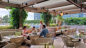 Un restaurante en la azotea con mesas al aire libre, plantas y vistas panorámicas de la ciudad.