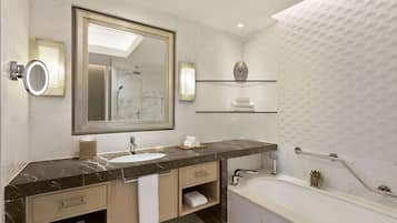 Een moderne badkamer met een marmeren wastafelmeubel, een grote spiegel, een inbouwgootsteen, een badkuip en een plank met toiletartikelen.