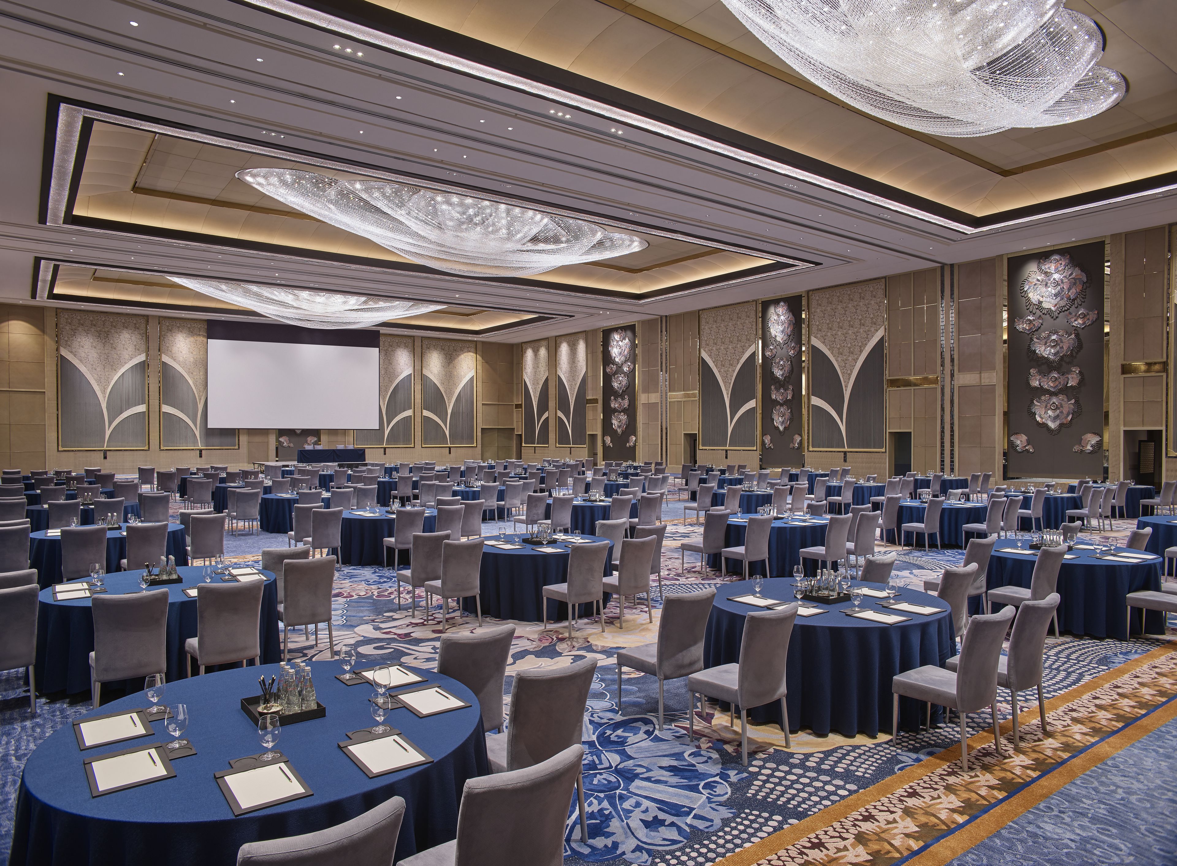 A large conference room with round tables, chairs, and a large screen.
