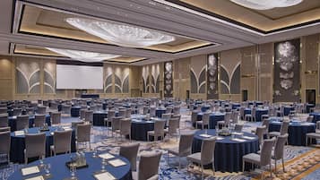 A large conference room with round tables, chairs, and a large screen.
