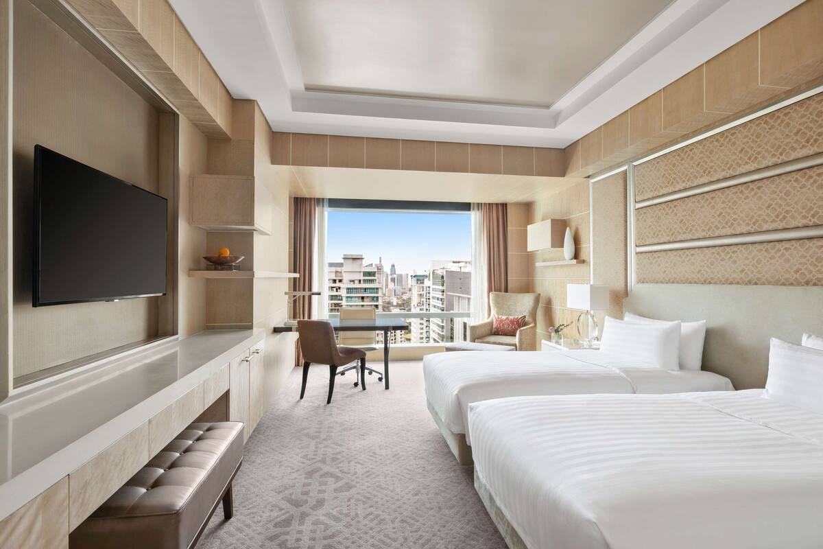Une chambre d’hôtel avec deux lits, une télévision, un bureau et une vue sur la ville.