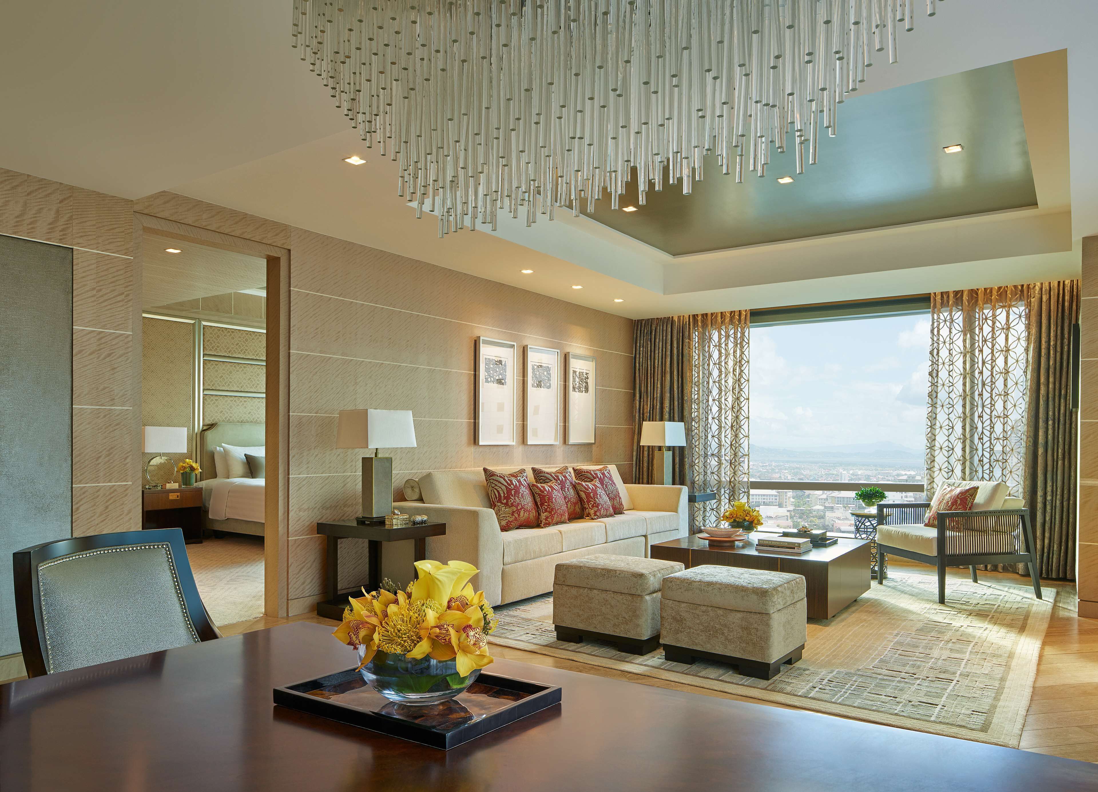 A modern hotel room with a large window, a sofa, a coffee table, and a dining table with a vase of flowers.