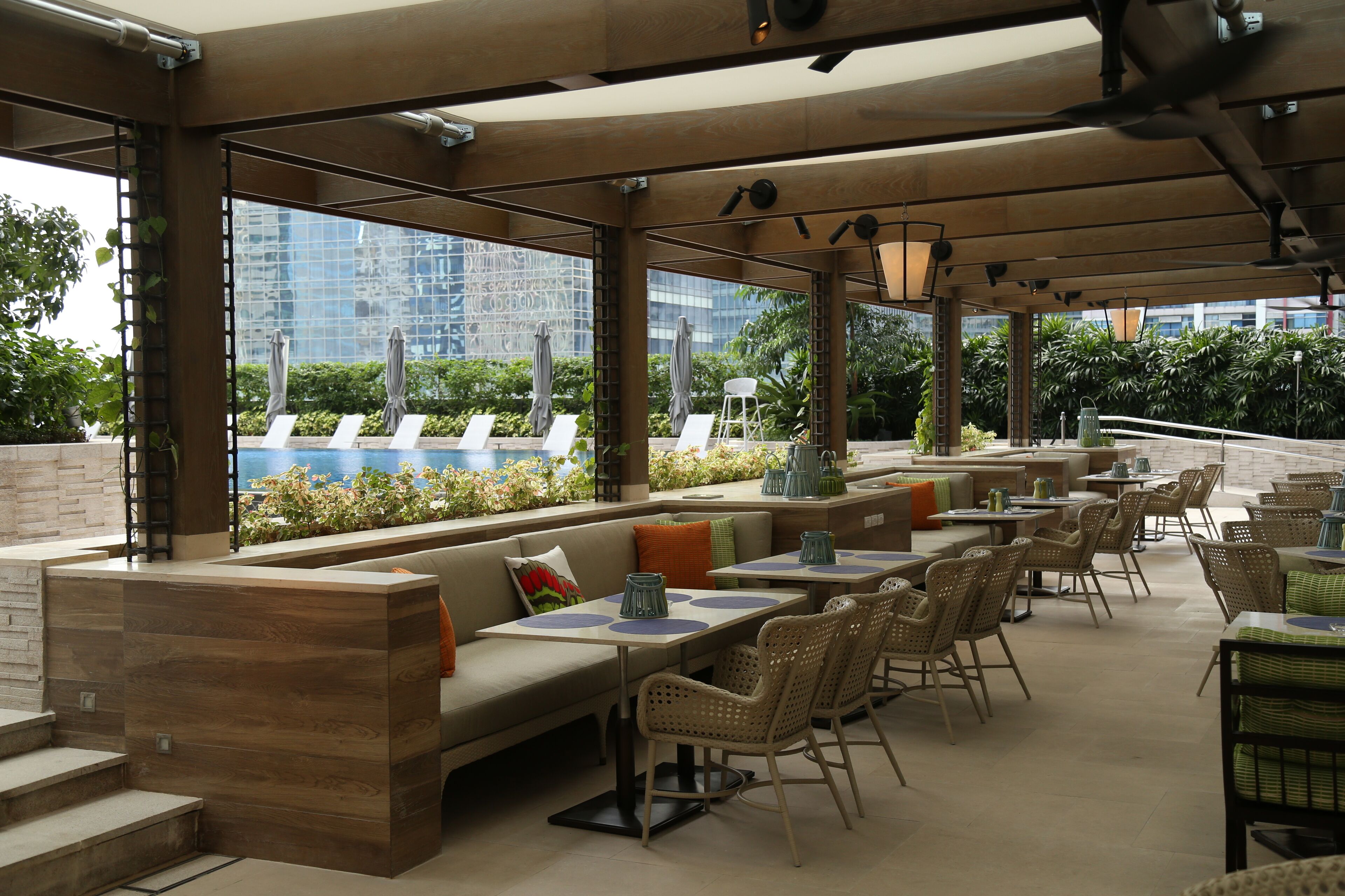 An outdoor seating area with tables and chairs, a wooden bench, and a view of a building and greenery.