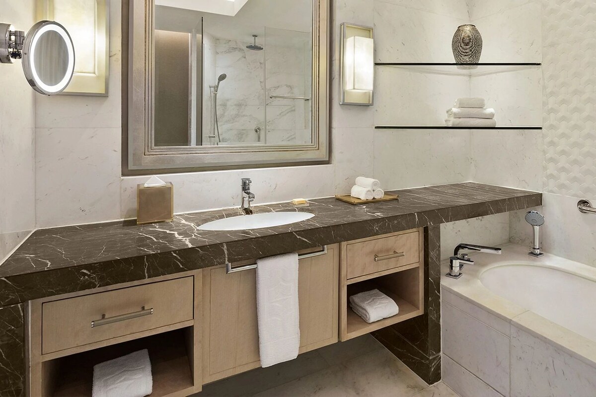 A modern bathroom with a marble countertop, a sink, a mirror, a shower, and a bathtub.
