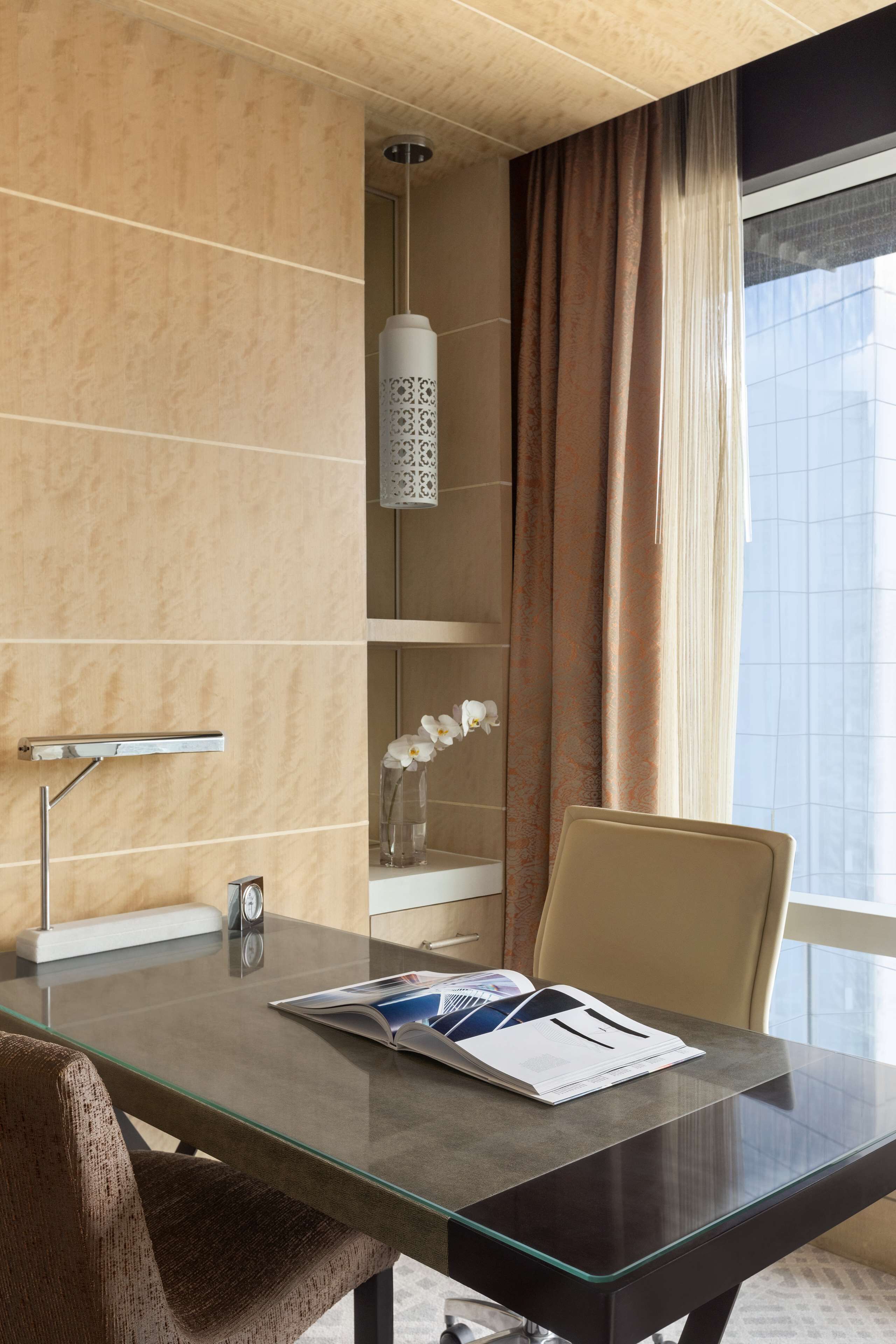 A modern hotel room with a glass table, a shower area, and a view of the city.